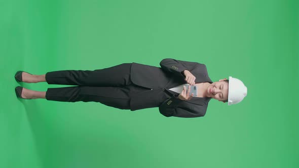 Full Body Of Asian Female Engineer With Safety Helmet Using Smartphone In The Green Screen Studio