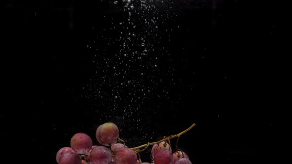 Slow Motion Red Grapes Falling Into Transparent Water on Black Background