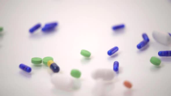Slow Motion Macro of Pill Varieties Sliding onto One Blue and Yellow Pill on White Background