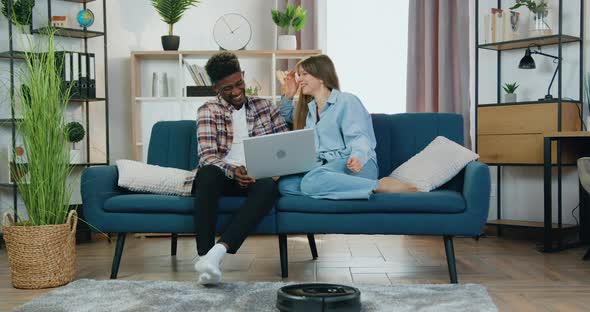 Guy and Girl Talking During Revision on Computer at Home while Robot Vacuum Cleaner