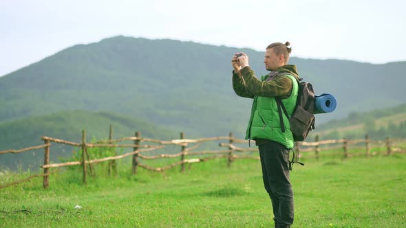 Young Man a Tourist with a Backpack Takes a Beautiful Picture on a Mobile Phone