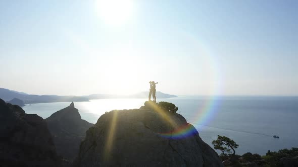 Aerial Silhouette of a Loving Couple Standing on the Top of a Mountain Over the Sea at Sunrise and