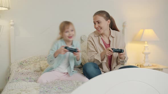 Joyful Woman and Little Girl Playing Video Game Celebrating Victory Having Fun in Bed