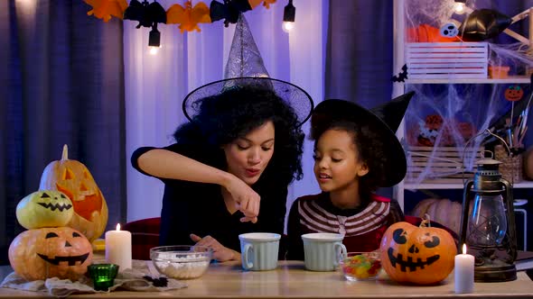 Mom and Daughter African American in Festive Costume and Witch Hat Having Fun and Drinking Hot