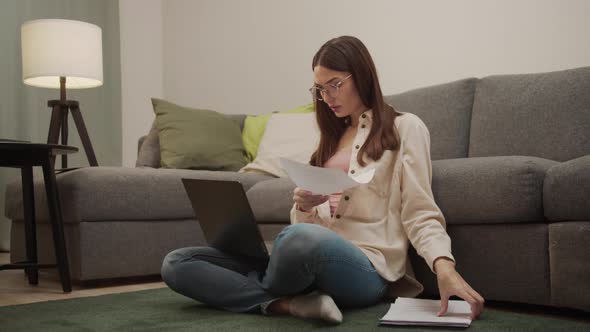 A Young Girl Sits on the Floor in the Living Room and Looks at the Documents