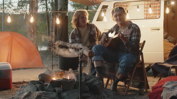 Young Couple Sitting to Guitar by Campfire