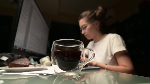 A young woman works at the computer at night and drinks coffee. Work at night