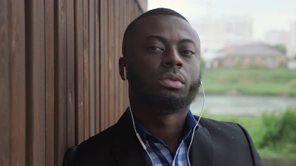 Black Man in Earphones is Listening Music at City Street During Rain