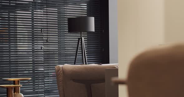 Black minimalist circular floor lamp next to a window with modern black blinds.