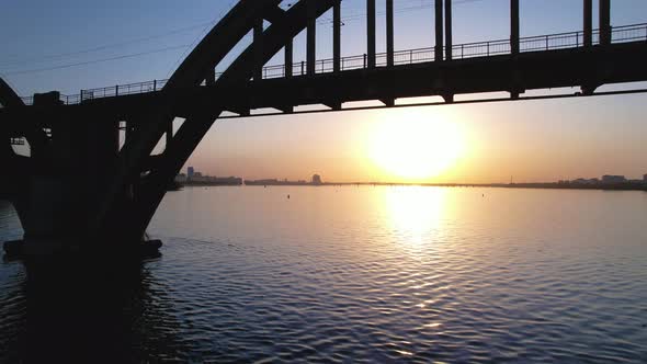 Beautiful sunset, sunrise over the river. Drone view, moving under the arch bridge. Dnipro, Ukraine.