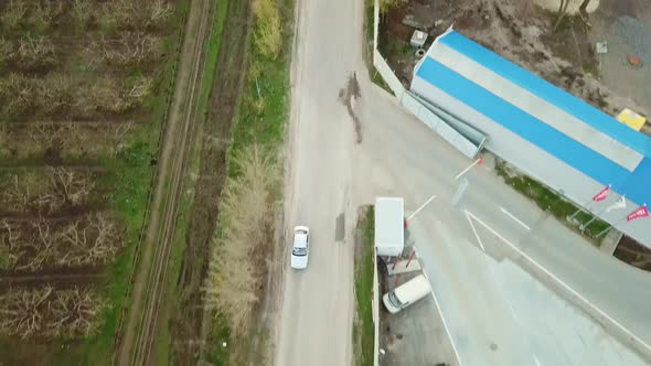 the Car Drives Along the Village Road Along Agricultural Buildings and Gardens