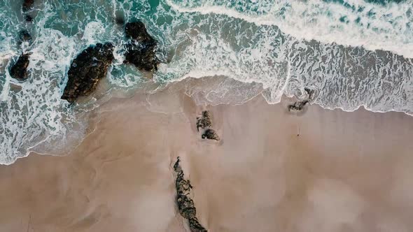 Above vertical view of blue ocean waves and yellow sandy beach
