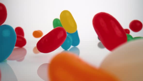 Camera follows jelly beans falling on surface. Slow Motion.