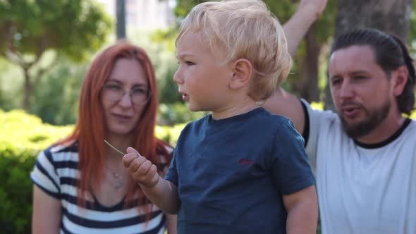 A Little Blonde Boy with His Parents in the Green Park