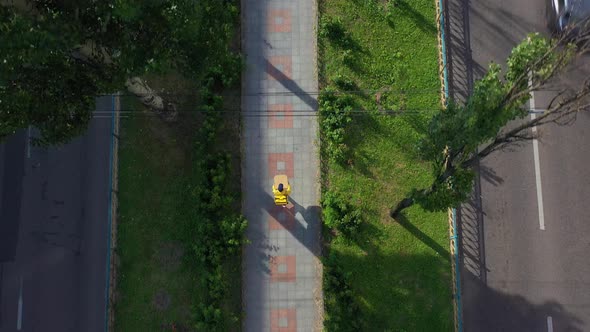 Aerial Top View of Food Delivery Courier with Yellow Uniform Holding Boxes of Pizza Walking Down the