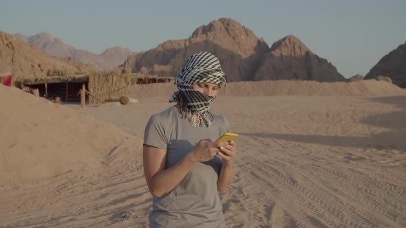 Female Tourist in Checkered Keffiyeh Standing in the Desert Using Mobile Phone