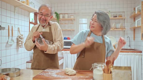 Asian Senior elderly Couple dancing together with happiness while cooking foods in kitchen at home.