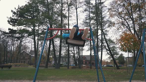 Boy is Swaying on Swing in Park at Autumn Day and Jumping Out in Slow Motion