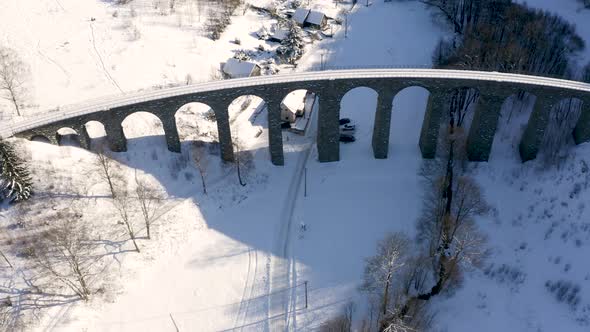 Stone train railroad viaduct towering above a small village,snowy.