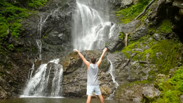 a Man Raises His Hands Up Against the Background of the Mervisi Waterfall in Georgia