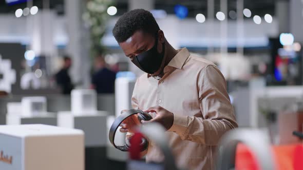 Young Black Guy is Viewing New Model of Wireless Headphones in Trading Hall of Audio Equipment Shop