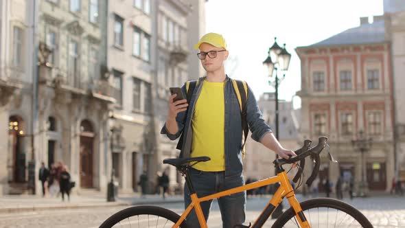 Portrait of a Happy Delivery Man Who is Standing and Texting on a Smartphone