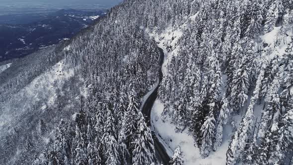 Aerial View of a Car Driving in a Desert Road Along Snowed Mountain Side