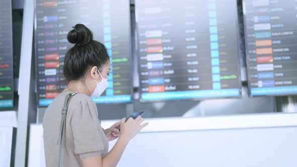 asian female traveller wearing face mask hand use smartphone checking map and flight schedule