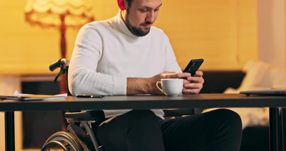 Male Millennial in Wheelchair Holding Modern Smartphone Texting Message in Office Young Businessman