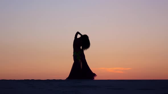 Girl Is Dancing Belly Dancing Against the Beautiful Sunset on the Beach. Silhouettes