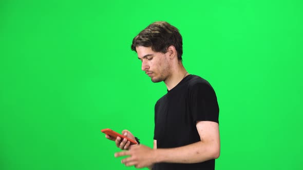 Brunette Man Goes and Texting with Smartphone on Green Screen at Studio.