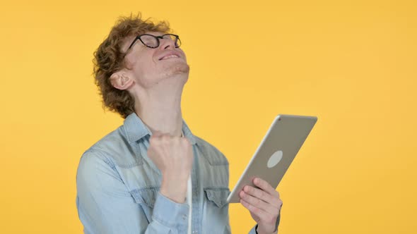Redhead Young Man Celebrating on Tablet, Yellow Background 