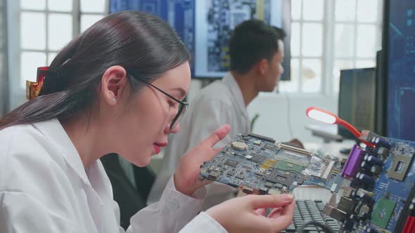 Development Facility: Beautiful Asian Female Engineer Inspects Printed Circuit Board Motherboard