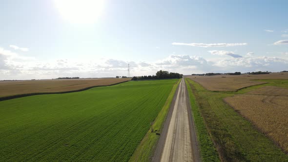 Panorama over farm field on top of hill. Sun glowing in the blue sky with gentle clouds.