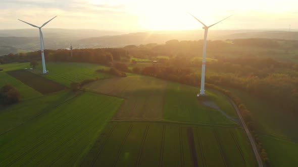 drone flight over green fields with wind turbines into the sunrise