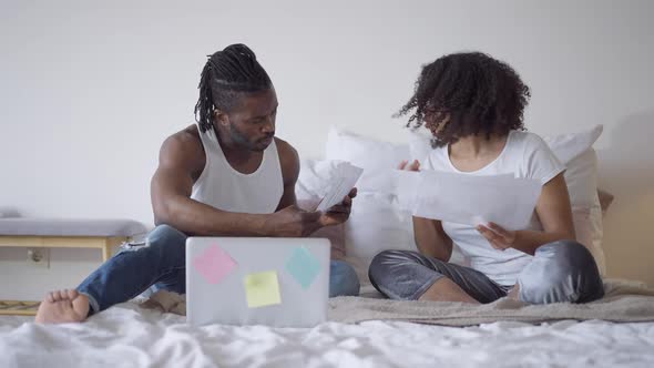 Wide Shot of Confident Successful African American Couple Analyzing Graphs Sitting on Bed at Home