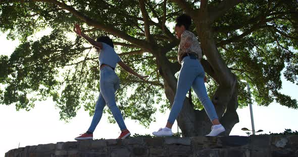 Two mixed race women walking on wall in park