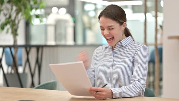 Excited Young Woman Celebrating Success on Documents in Office 