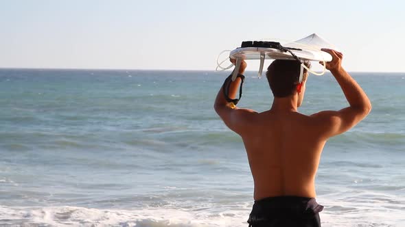 A young man holding his surfboard on the beach.