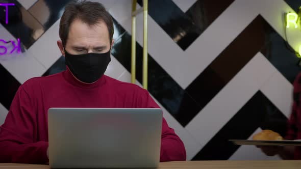 Waiter in Black Protective Mask Brings Coffee and Croissant to Middleaged Man