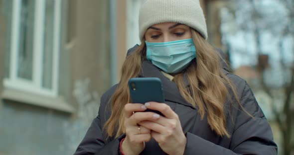 Portrait of Woman in Medical Protective Mask Typing By Mobile Phone Outdoors. Close Up Cheerful Girl