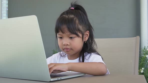 Asian girl student holding a pen for taking notes and doing homework and using the laptop