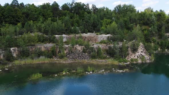 Aerial View of lake with Beautiful Water in a Quarry Surrounded by Forest Tracking Backward