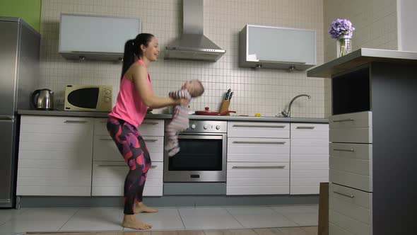 Happy Fit Mother Doing Squats Lifting Baby at Home