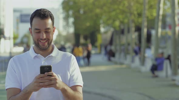 Smiling Young Brunet Using Smartphone Outdoor