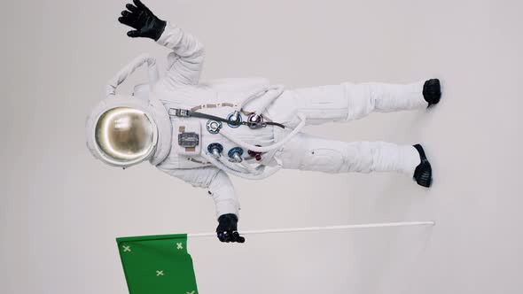 Astronaut Stands with a Flag on a Light Background and Waves His Hand