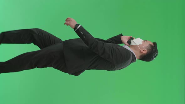 Asian Business Man Talking On Mobile Phone While Walking On Green Screen, Wear Medical Mask