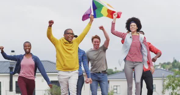 Happy group of diverse male and female protesters walking with rainbow flag