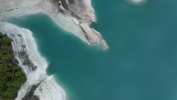 Forward Aerial of Still Lake Trees and Eroded Stony Coastline Spain