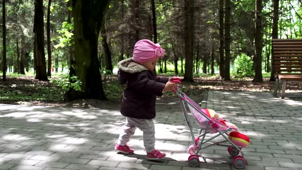 Baby girl walking with her stroller toy in spring park alt